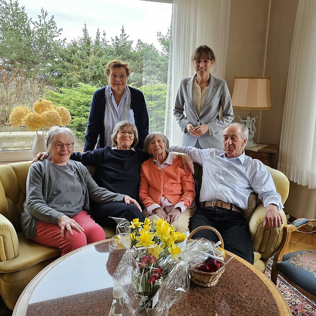 Antonie Hüttner, auf einem Sofa sitzend, mit Oberbürgermeisterin Eva Döhla, Verwandten und Nachbarn um sie herum
